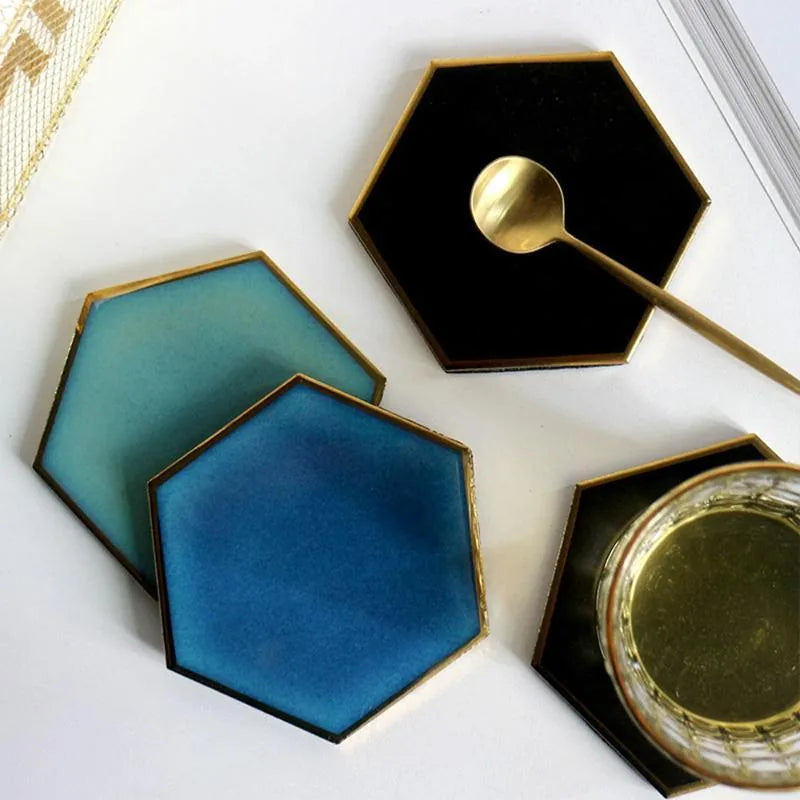 Quatre dessous de verre hexagonaux de couleurs différentes disposés en éventail, avec une cuillère dorée et un bocal doré sur l'un d'eux.