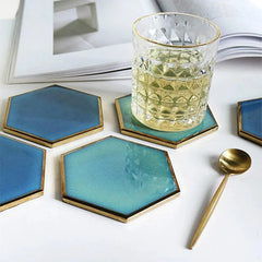 Deux dessous de verre hexagonaux bleus sous un verre de cocktail pétillant, avec une cuillère dorée et un magazine en arrière-plan.