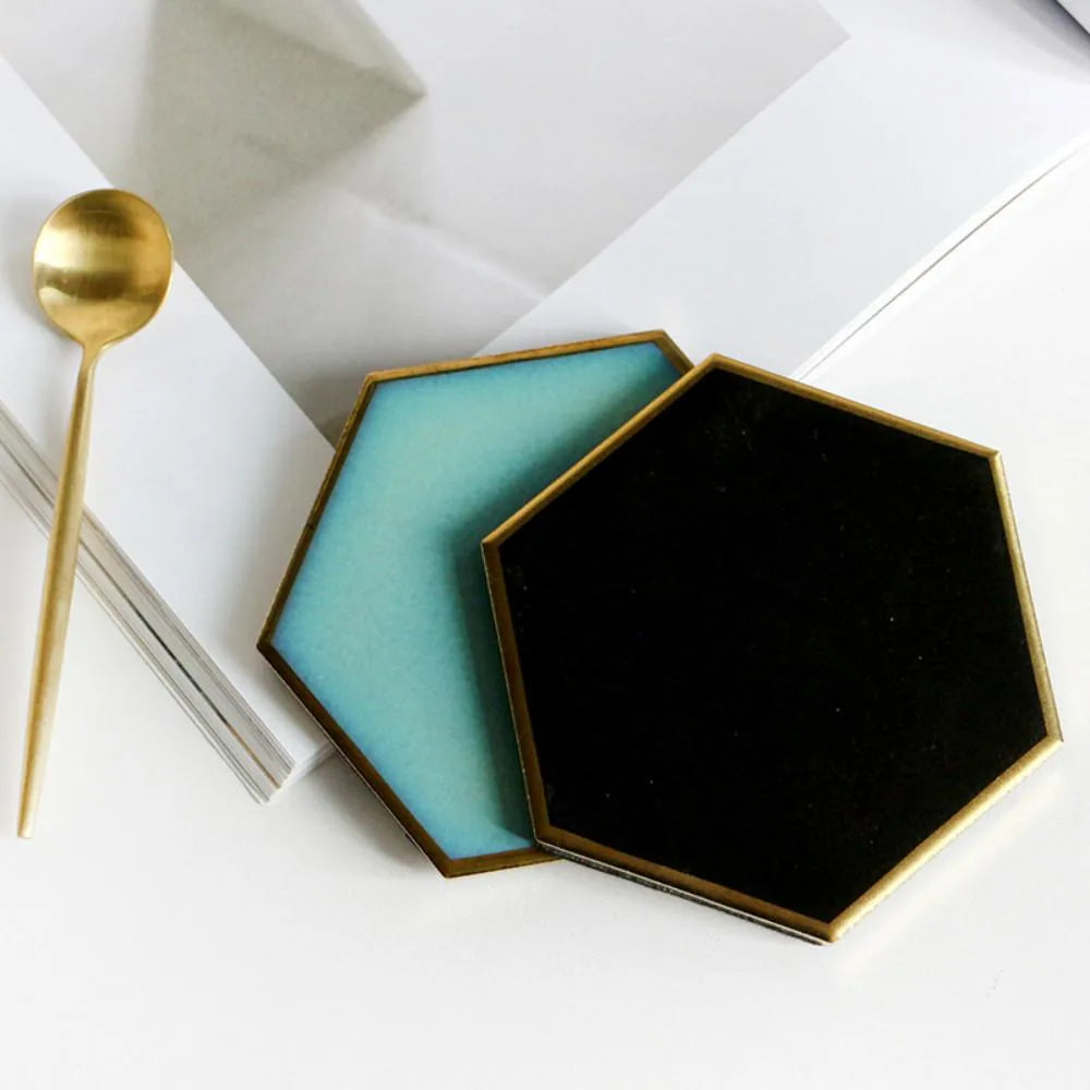 Deux dessous de verre hexagonaux superposés, l'un turquoise et l'autre noir, avec une cuillère dorée posée à côté.