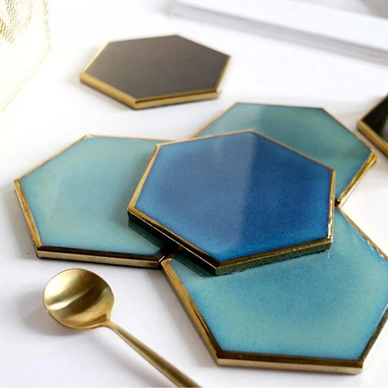Gros plan sur trois dessous de verre hexagonaux (noir, bleu turquoise et bleu profond) avec une cuillère dorée posée dessus.