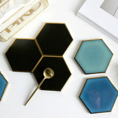 Vue du dessus d'une collection de dessous de verre hexagonaux noirs et bleus, disposés à côté d'une corbeille dorée et d'un magazine.