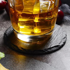 Dessous de verre en ardoise noire sous un verre de whisky avec glaçons, cerises en arrière-plan