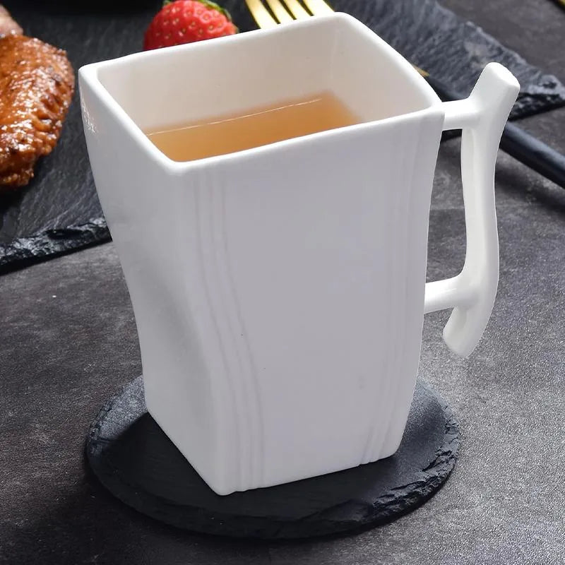 Dessous de verre en ardoise sous une tasse de thé blanche, avec une collation sucrée-salée en arrière-plan