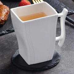 Dessous de verre en ardoise sous une tasse de thé blanche, avec une collation sucrée-salée en arrière-plan