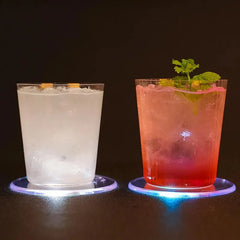 Deux verres de cocktails, l'un trouble avec glaçons et l'autre rosé garni de menthe fraîche, chacun posé sur un dessous de verre lumineux bleu.