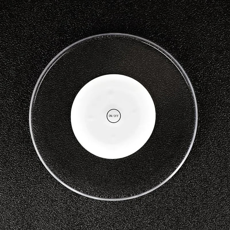 Vue de dessus du dessous de verre lumineux transparent avec base blanche centrale et bouton marche-arrêt, posé sur une surface noire texturée.