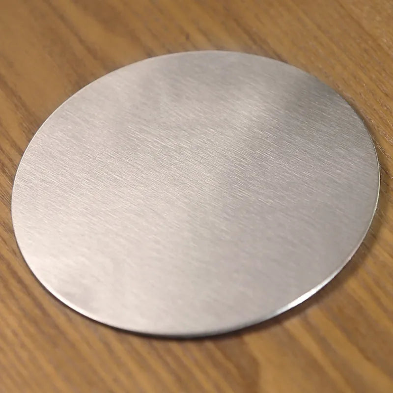 Dessous de verre rond en métal inox brossé posé seul sur une table en bois, vue rapprochée de la texture.