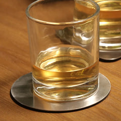 Gros plan sur un verre de whisky posé sur un dessous de verre rond en métal, avec un second verre flou en arrière-plan.