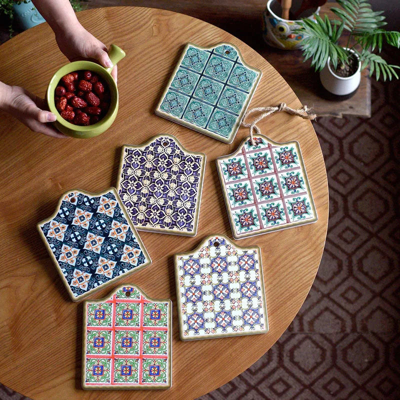 Six dessous de verre en mosaïque aux motifs variés disposés sur une table en bois, avec des mains tenant un bol de fruits rouges.