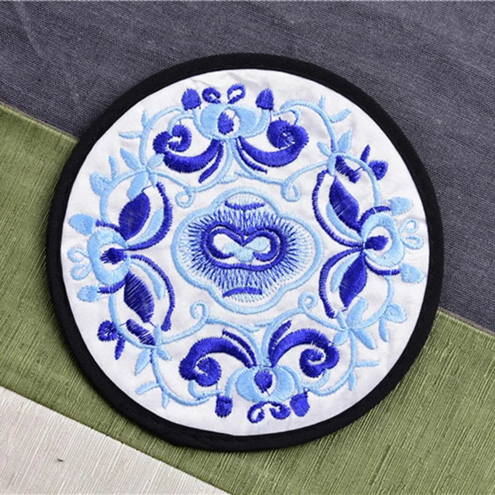 Dessous de verre en tissu brodé blanc à motif floral bleu roi vu en gros plan sur un tissu gris et vert.