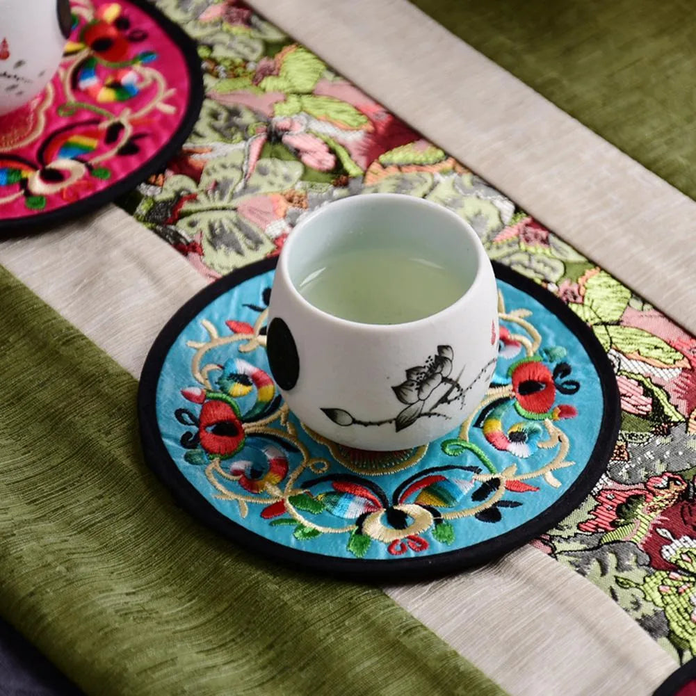 Tasse de thé posée sur un dessous de verre en tissu brodé turquoise sur un chemin de table.