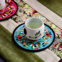Tasse de thé posée sur un dessous de verre en tissu brodé turquoise sur un chemin de table.