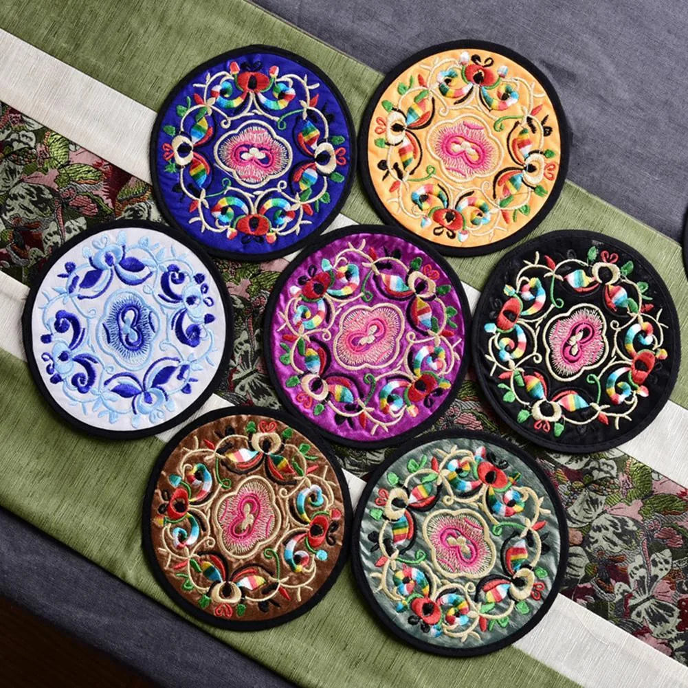 Pile de sept dessous de verre en tissu brodé de coloris différents empilés en éventail sur un chemin de table.