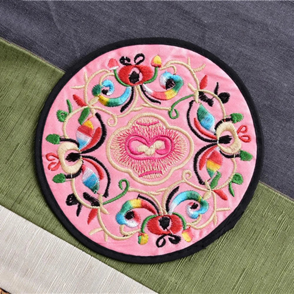 Dessous de verre en tissu brodé rose pâle à motif floral multicolore vu en gros plan.