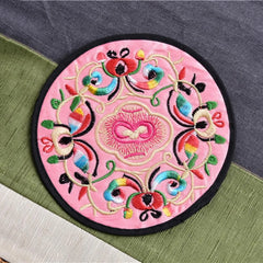 Dessous de verre en tissu brodé rose pâle à motif floral multicolore vu en gros plan.