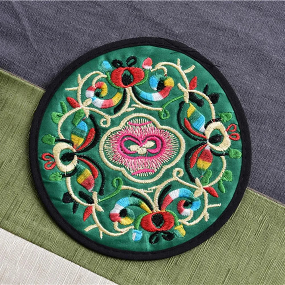 Dessous de verre en tissu brodé vert émeraude à motif floral multicolore vu en gros plan.