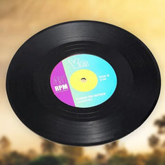 Dessous de verre en forme de vinyle 45 tours, vue inclinée montrant l'étiquette centrale colorée sur fond beige.