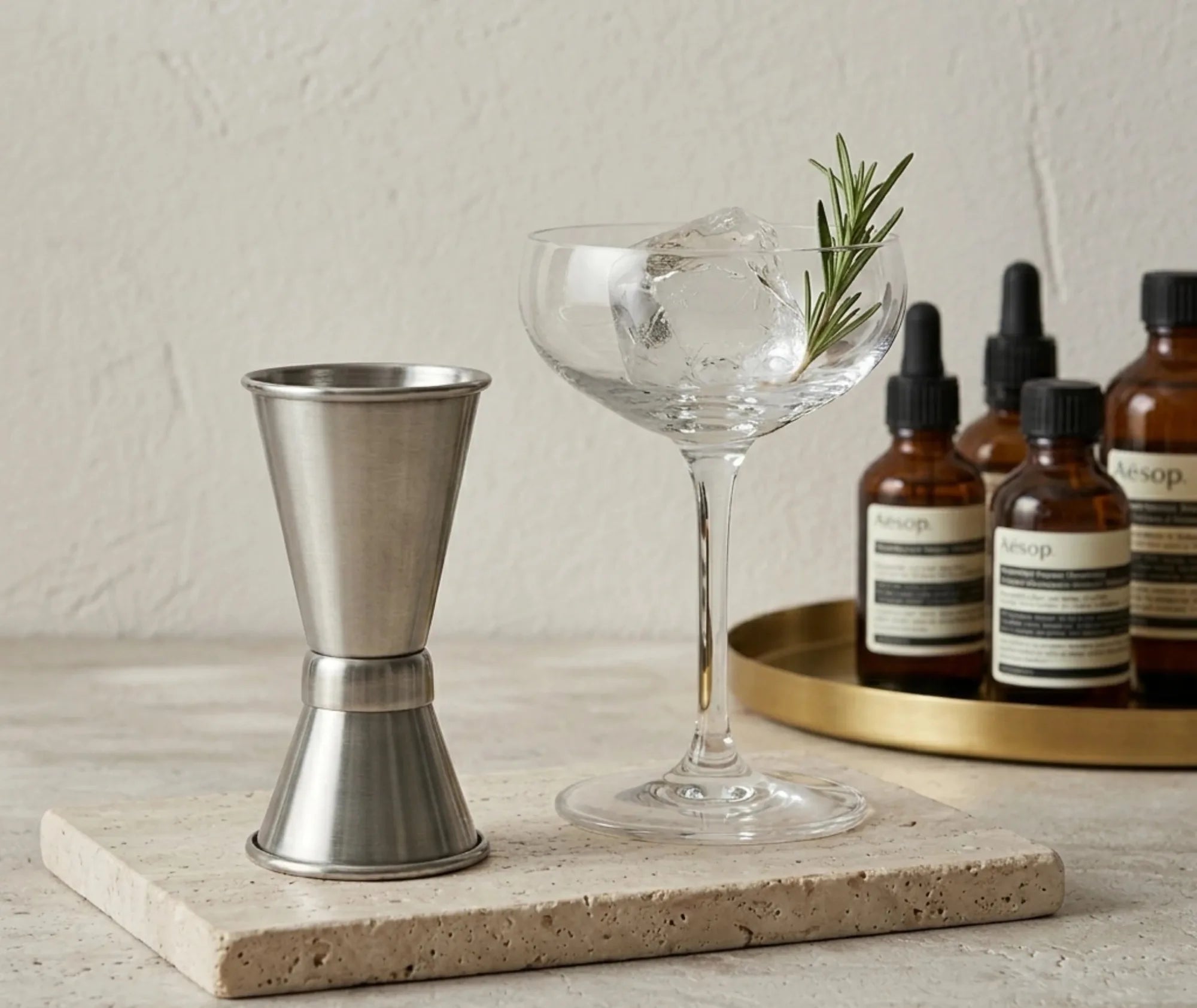 Doseur à alcool cocktail posé sur une plaque en pierre à côté d'un cocktail glaçon et romarin