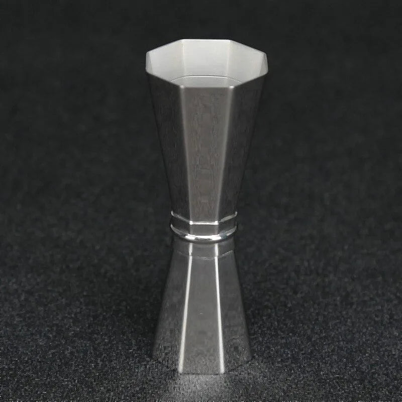 Doseur à cocktail en inox debout sur fond noir, mettant en valeur ses reflets métalliques et sa silhouette diabolo.