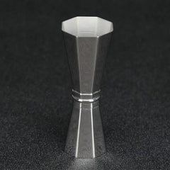 Doseur à cocktail en inox debout sur fond noir, mettant en valeur ses reflets métalliques et sa silhouette diabolo.