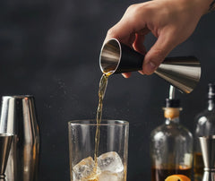 Doseur professionnel versant un alcool ambré dans un verre rempli de glaçons, ambiance de bar sombre