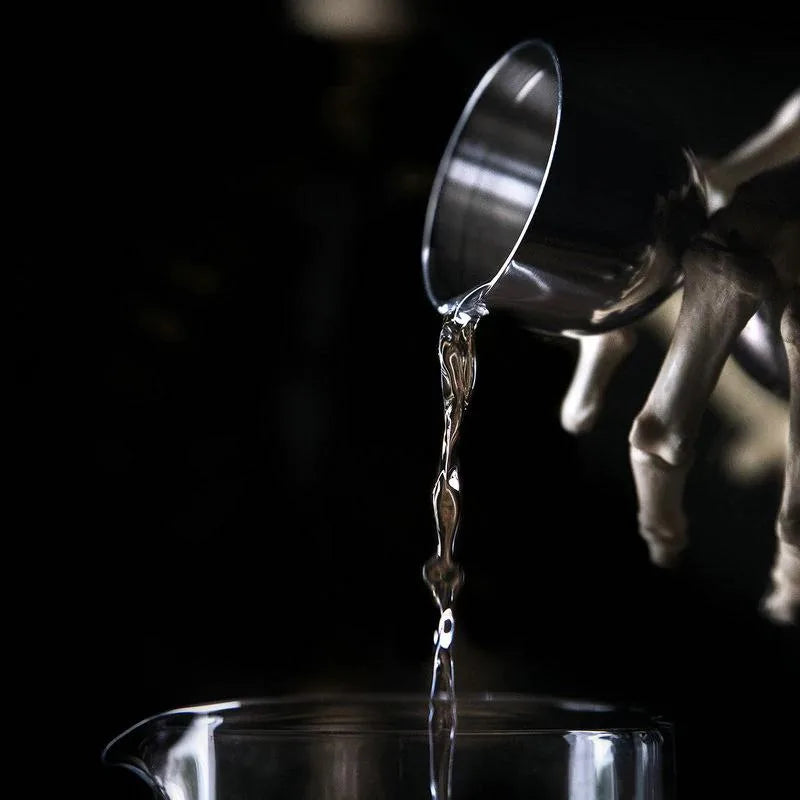 Gros plan artistique d'un doseur à cocktail versant un liquide transparent dans un verre à mélange sur fond noir.