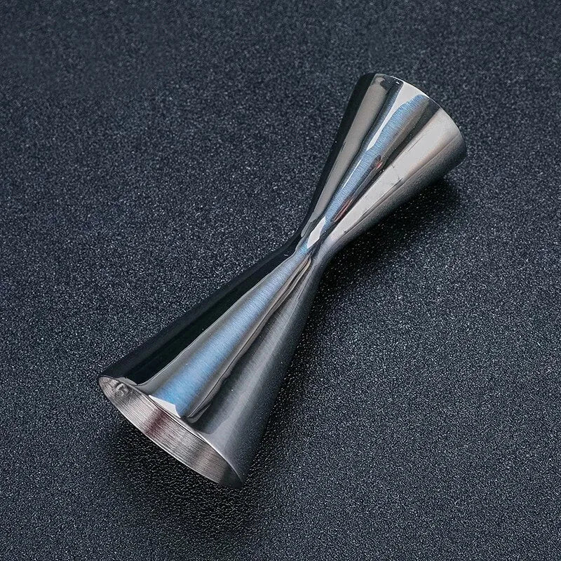 Doseur à cocktail en inox poli couché sur fond noir, mettant en valeur les reflets métalliques
