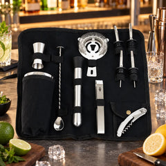 Trousse de bar en toile noire posée à plat entourée de citrons, citrons verts, glaçons et menthe fraîche sur un comptoir