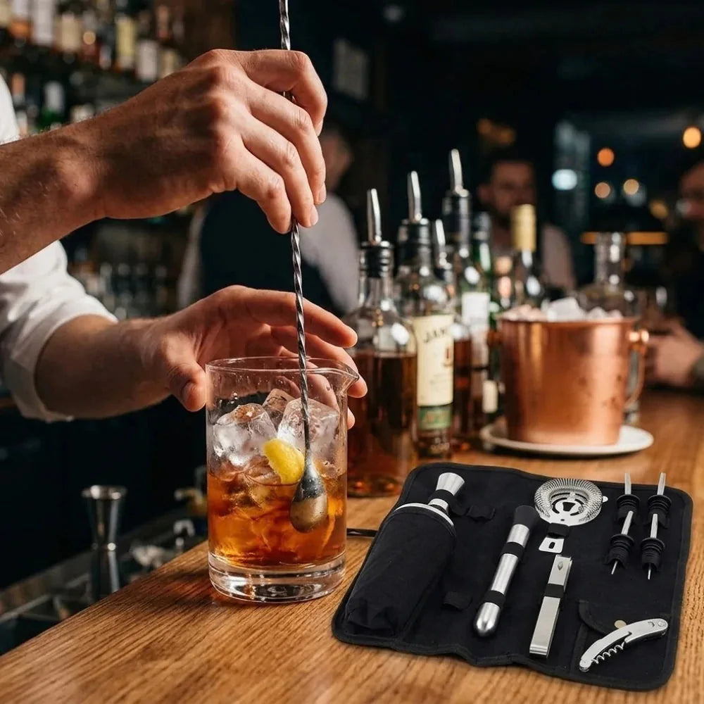 Barman préparant un cocktail à la cuillère de mélange torsadée, avec la trousse d'accessoires posée sur le comptoir