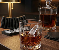 Gros plan sur un glaçon en forme de balle dans un verre de whisky, avec une carafe en cristal en arrière-plan