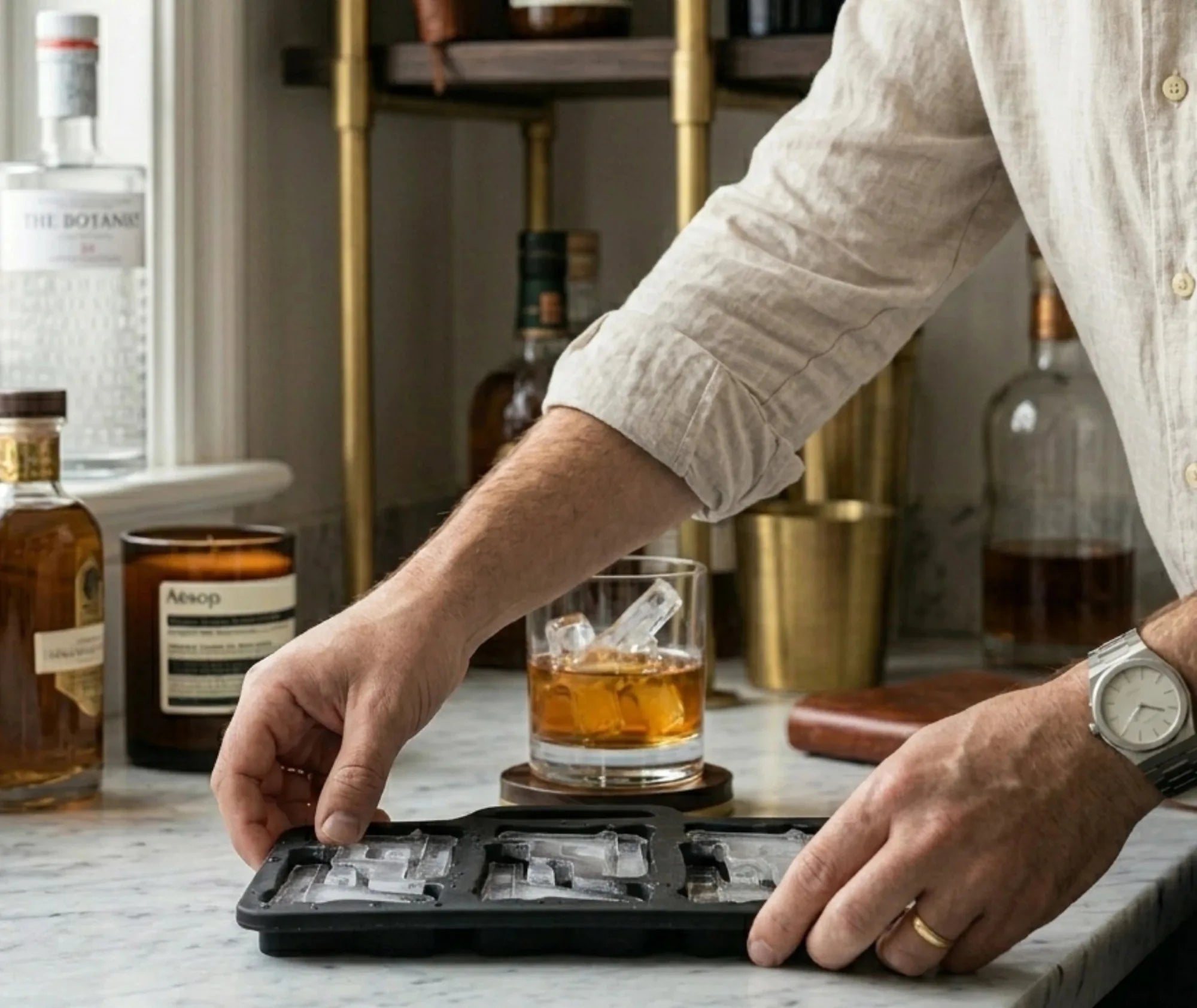 Un homme démoule des glaçons en forme de pistolet du moule Kit Cocktail Shop dans un bar chic, avec des bouteilles de spiritueux en arrière-plan