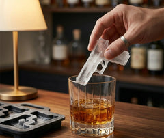Gros plan d'une main plaçant un glaçon en forme de pistolet dans un verre de whisky, ambiance bar tamisée avec lampe dorée