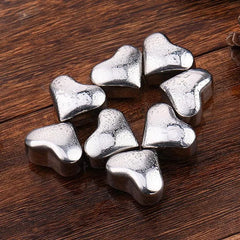 Plusieurs glaçons coeur en inox couverts de gouttes de condensation, disposés en cercle sur du bois foncé.