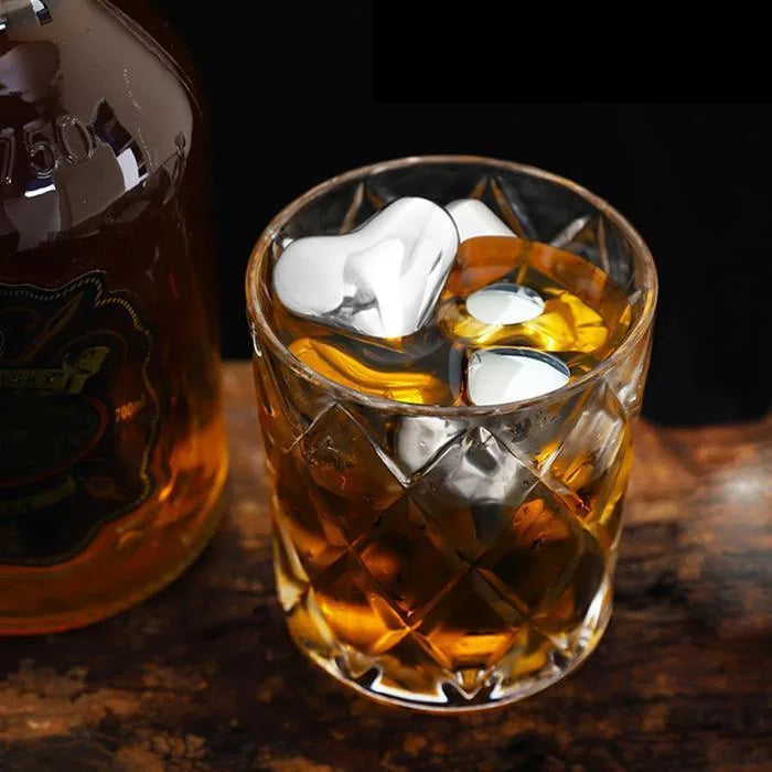 Glaçons coeur en inox plongés dans un verre de whisky taillé, bouteille en arrière-plan.