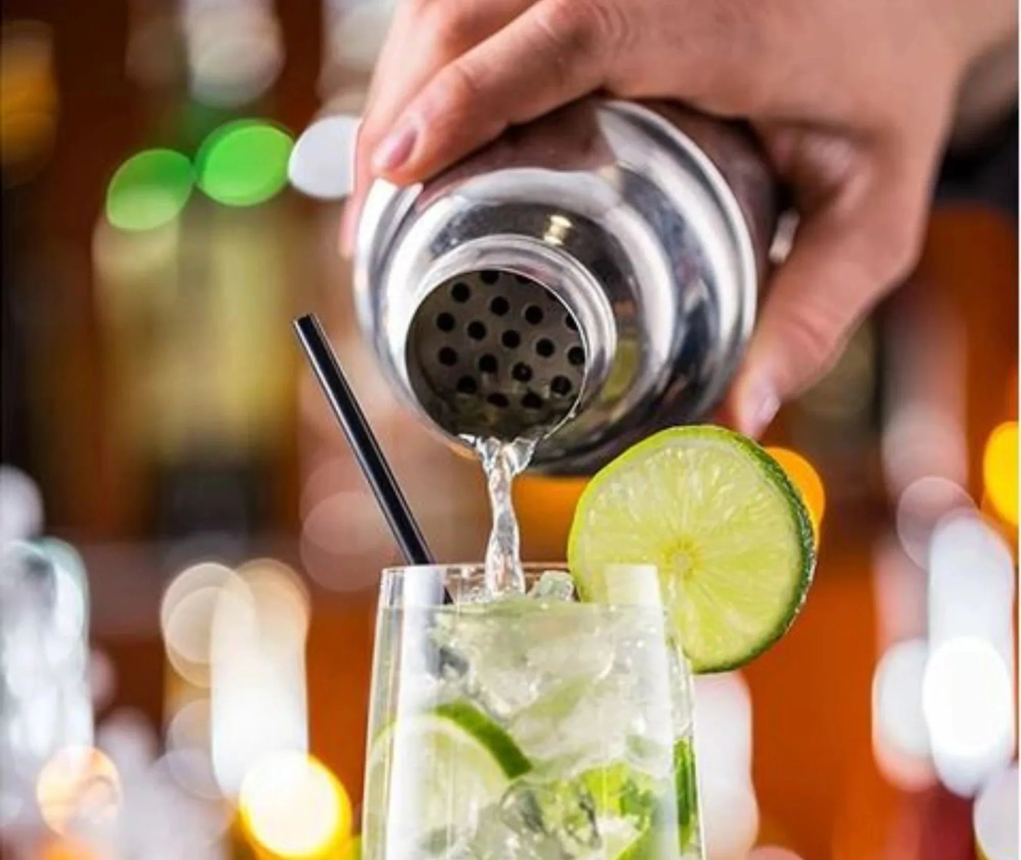 Gros plan sur le shaker du kit cocktail en bois versant un mojito glacé garni de citron vert dans une ambiance de bar.