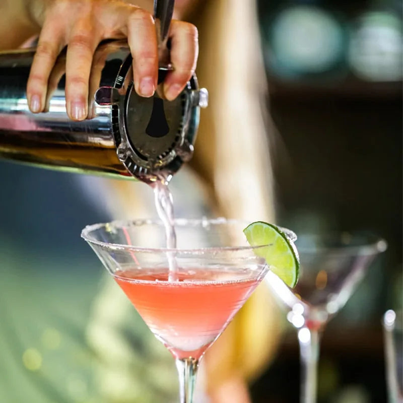 Service d'un cocktail rose filtré à la passoire Hawthorne dans un verre à martini garni d'une rondelle de citron vert