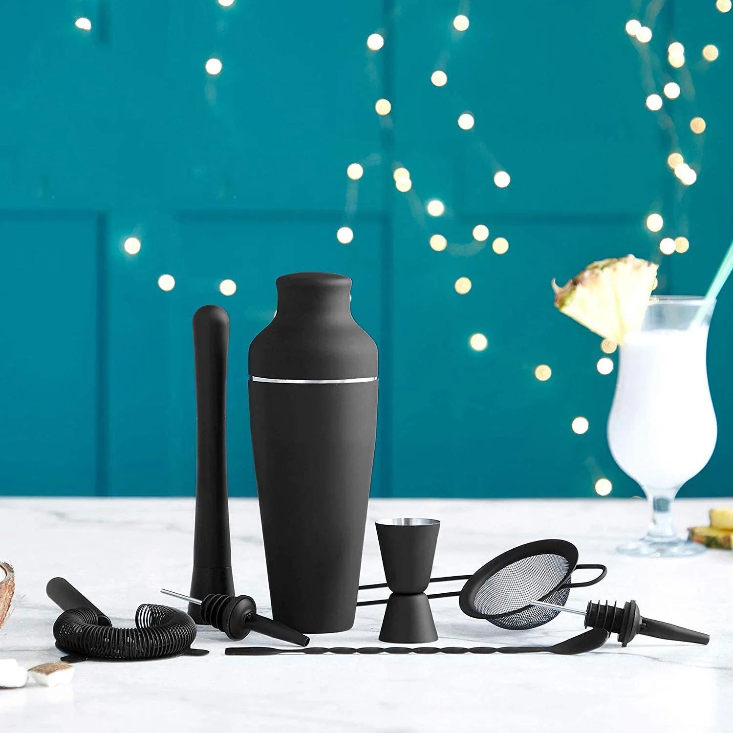Kit cocktail débutant posé sur un plan de travail avec ambiance bar tropical, guirlande lumineuse et cocktail à l'ananas en arrière-plan
