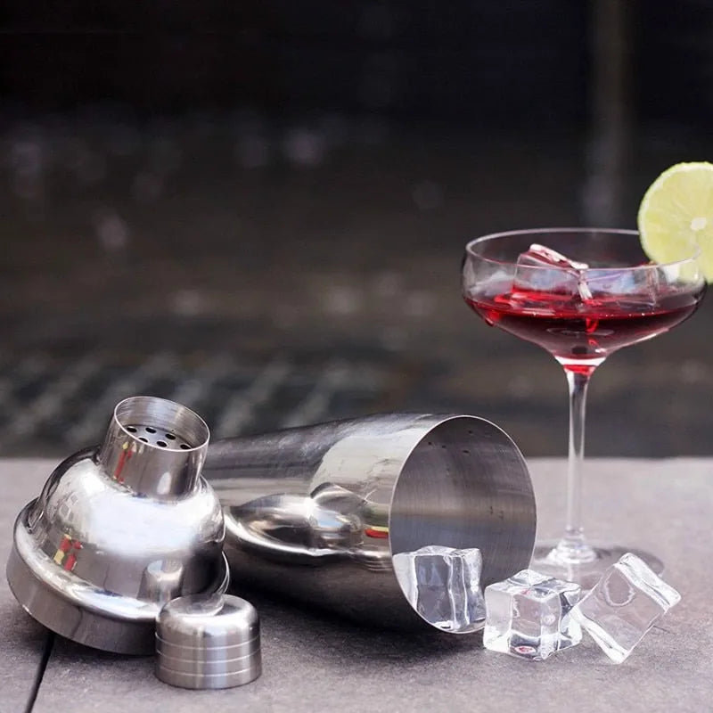 Shaker du kit cocktail démonté posé près d'un cocktail rouge garni de glaçons et d'une rondelle de citron vert