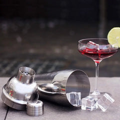 Shaker du kit cocktail démonté posé près d'un cocktail rouge garni de glaçons et d'une rondelle de citron vert
