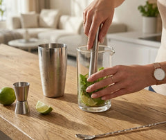 Préparation d'un mojito à la menthe avec les accessoires du kit cocktail, sur un plan de travail en bois