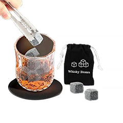 Une pierre à whisky saisie à la pince est plongée dans un verre de whisky posé sur un sous-verre, avec la pochette Whisky Stones et deux pierres supplémentaires à côté