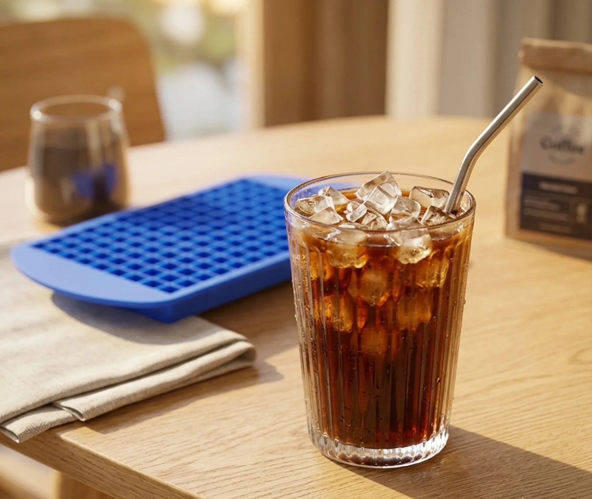 Moule à glaçons petits cubes bleu posé sur une table en bois, à côté d'un verre de boisson glacée avec une paille en inox.
