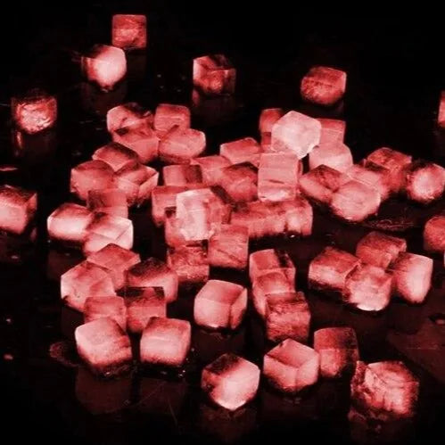 Gros plan sur de nombreux petits glaçons translucides éclairés en rouge, dans une ambiance sombre et festive.