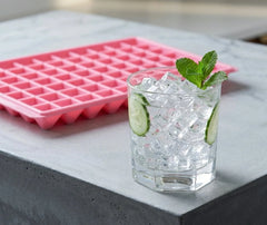 Moule à mini glaçons rose posé à côté d'un verre de cocktail glacé garni de concombre et de menthe