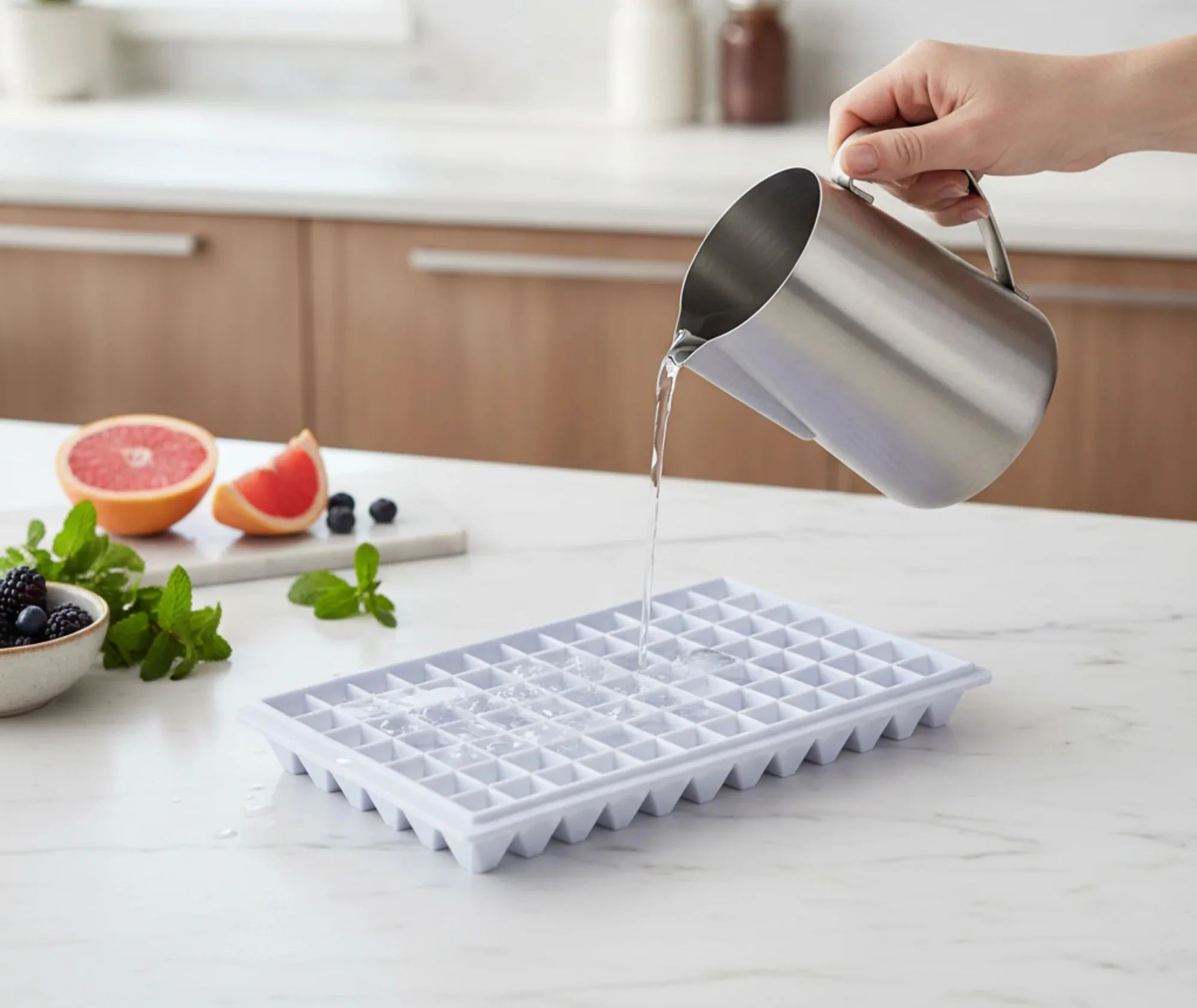 Remplissage d'un moule à mini glaçons lavande avec de l'eau dans une cuisine, entouré de fruits frais
