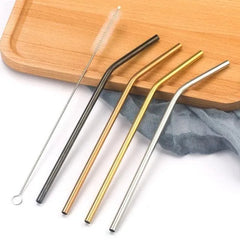 Pailles à cocktail en inox courbées de quatre couleurs différentes disposées en diagonale sur une planche en bois clair, à côté d'un linge gris et du goupillon de nettoyage.