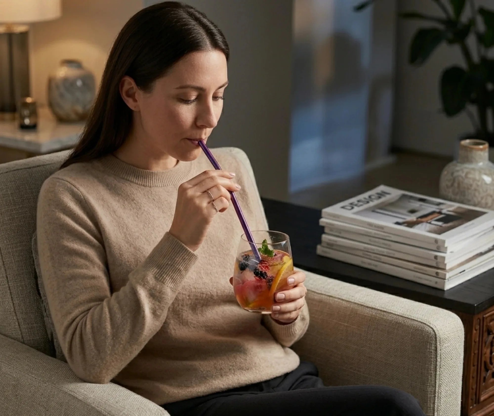 Femme assise dans un fauteuil buvant un cocktail aux fruits avec une paille en métal violette