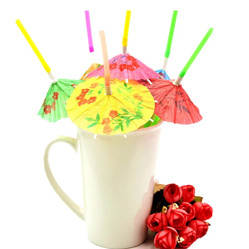 Assortiment de pailles cocktail à parasol colorées plantées dans une tasse blanche, à côté d'un bouquet de fleurs rouges artificielles
