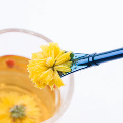 Gros plan sur l'embout filtrant bleu d'une paille à mojito retenant une fleur comestible dans une boisson ambrée.