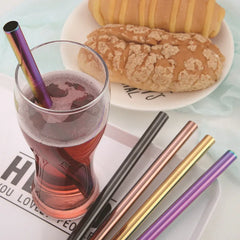Verre de boisson rouge glacée avec une paille irisée, posé sur un plateau avec des pailles colorées et des viennoiseries en arrière-plan